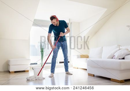 people, housework and housekeeping concept - happy man in headphones with mop cleaning floor at home