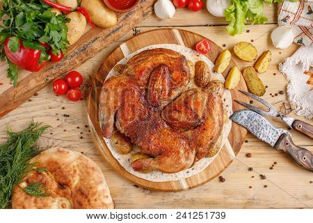 Chicken With Potato Garnish On A Round Wooden Board. Still Life With Textiles And Original Cutlery.