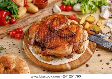 Juicy Tobacco Chicken With Potato Garnish On A Round Wooden Board.