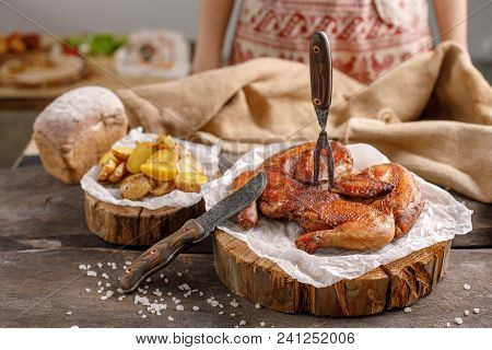 An Appetizing Chicken With A Fork Stuck Into It And A Potato Garnish On Wooden Spills. Still Life Wi