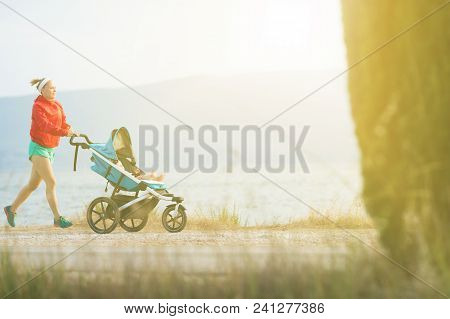 Running Super Mother With Child In Baby Stroller Enjoying Sunset And Mountains Landscape. Jogging Or