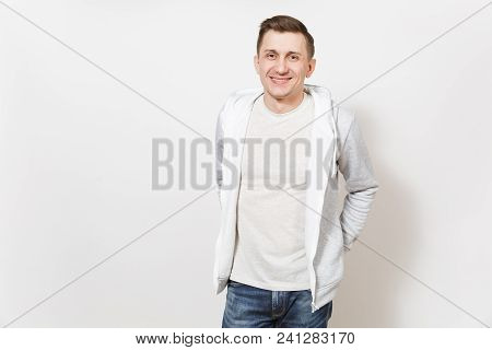 Young Handsomeman In T-shirt, Blue Jeans, Light Sweatshirt Holds His Hands In Jeans Pockets And Smil