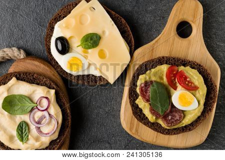 Open  faced  sandwich canape or crostini on a wooden serving board on dark stone background closeup. Top view.