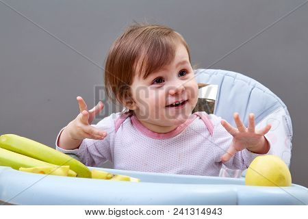 Portrait Of Adorable Toddler Girl Having Fun While Eating Friuts, Sitting In White And Grey Feeding 