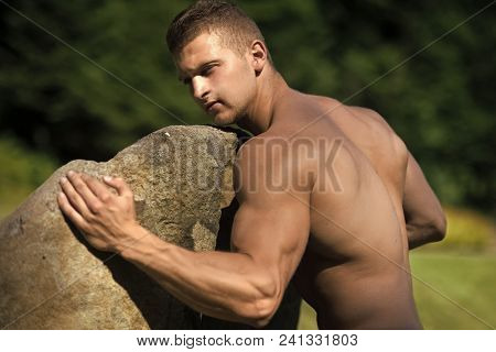 Handsome Man Face. Man Bodybuilder With Muscular Torso, Biceps, Triceps Push Stone On Sunny Summer D