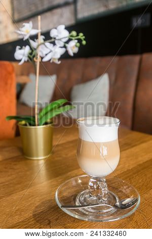 A tall glass of cappucinno or cafe latte served on a saucer with a thick white foam