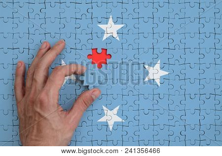 Micronesia Flag  Is Depicted On A Puzzle, Which The Man's Hand Completes To Fold