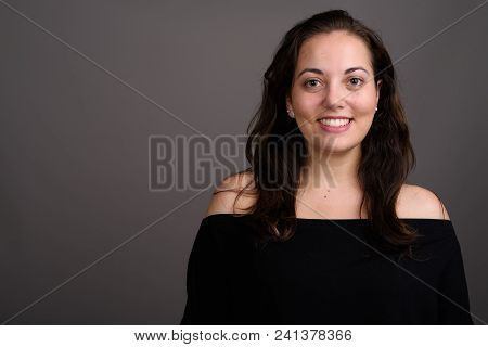 Studio Shot Of Young Happy Beautiful Woman Smiling While Wearing Black Off-shoulder Top Against Gray