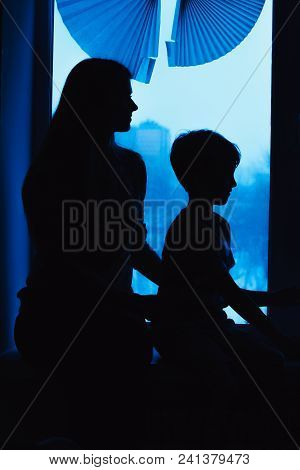Parents And Kids Sitting Near Window And Having Fun At Home. Silhouette View. Mother And Son On The 