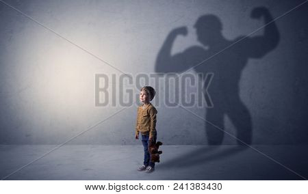 Little waggish boy in an empty room with musclemen shadow behind