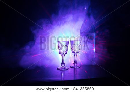 Two Glasses Of Vodka With Bottle On Dark Foggy Club Style Background With Glowing Lights (laser, Sto