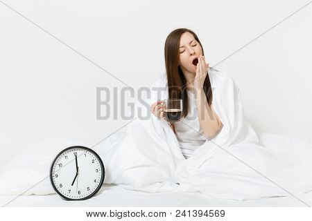 Tired Sad Woman Sitting In Bed With Cup Of Coffee, Round Clock, White Sheet, Pillow, Wrapping In Bla