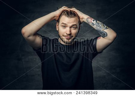 A Positive Hipster Male Dressed In A Black T Shirt Holds Head With Tattooed Arms.