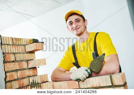 Bricklayer. Portrait of young smiling construction mason near brick wall