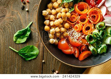 Colorful Buddha Bowl With Chickpeas, Carrots, Tomatoes, Cucumbers, Radish And Peppers On A Wooden Ta