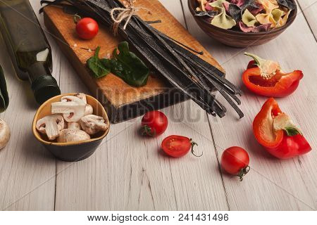 Cooking Pasta Background. Black Colored Fettuccine With Cuttle Fish Ink, Vegetables And Spices On Wh