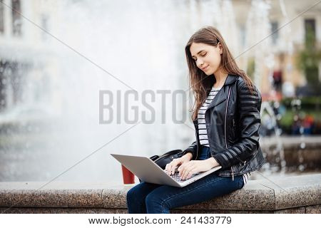 Young Woman Student Girl With Her Laptop Sitting On The Fontain