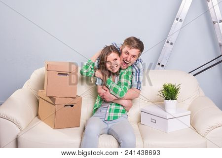 Happy Young Couple Sitting On The Floor In New Apartment After Moving In And Looking At Camera