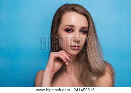 Beautiful Young Girl With Bright Pink Make-up And Combed Hair On A Blue Background Looks Into The Fr
