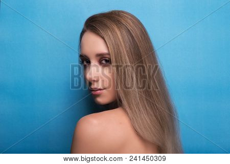 Beautiful Young Girl With Bright Pink Make-up And Combed Hair On A Blue Background Looks Into The Fr