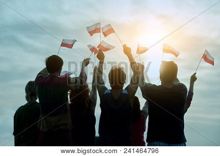 Poland Patriotic People With Small Flags, Back View. Blue Morning Sky Background.