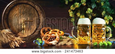 Oktoberfest beer barrel and beer glasses with soft pretzels, wheat and hop on rustic wooden table