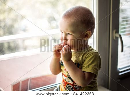 Sad Little Boy Sitting Near Window And Looking Outside
