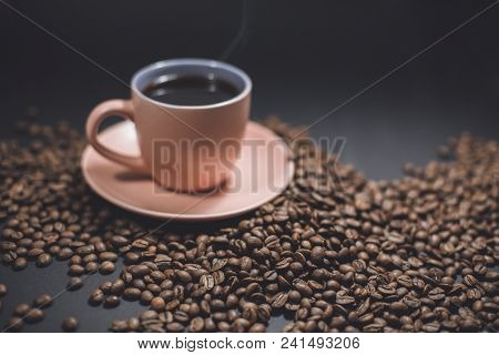 Cup Of Black Steaming Coffee On A Spilled Roasted Coffee Beans On A Black Background.