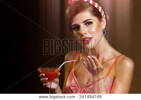 Pin up girl drink bloody Mary cocktail. Pin-up retro female style. Girl pin-up style wearing red dress. Invitation to party on Internet. Sepia.