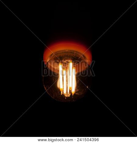 The Dim Light Of The Led Spiral In The Light Bulb With A Barely Visible Patron Is Gloomily Shining I