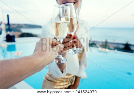 Woman and man clinking glasses at elegant pool party in summer
