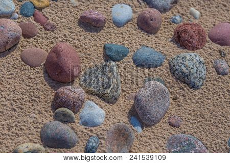 Beautiful Smooth Sea Stones In The Sands Of The Beach. Closeup Photo Of Stone Textures And Shapes.