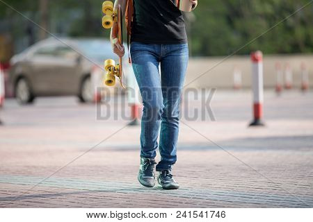 Walking With Skateboard And Coffee Themo Cup In Hand On City Street