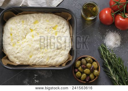 Cooking Focaccia Bread Or Pizza. Raw Focaccia With Ingredients On The Table, Tomatoes, Olives, Rosem