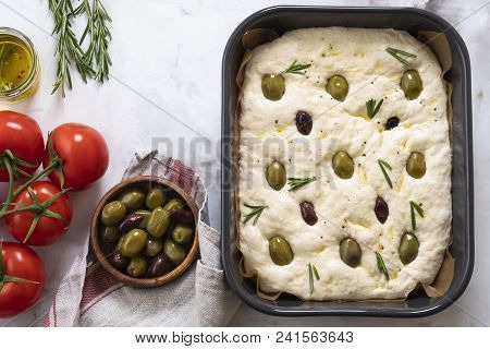 Cooking Focaccia Bread Or Pizza. Raw Focaccia With Ingredients On The Table, Tomatoes, Olives, Rosem