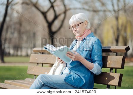 Avid Reader. Involved Blond Woman Reading A Book While Sitting On The Bench