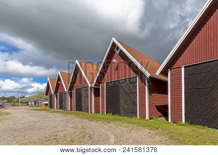 Traditional Swedish Wooden Storehouses In Red Color Under Clouded Summer Sky