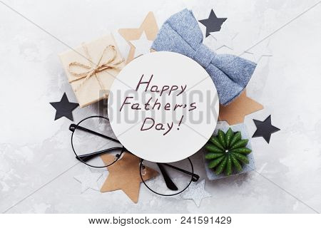 Happy Fathers Day Card Decorated Bowtie, Eyeglasses, Gift Box And Stars On Stone Table Top View In F
