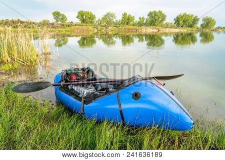 a blue pacraft (one-person light raft used for expedition or adventure racing) with a kayak paddle on a lake shore in spring scenery