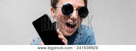 Young Girl In Round Glasses On A Gray Background. Portrait Of A Young Beautiful Girl. Charming Girl 