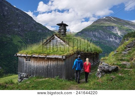 Kagefla - historic mountain farms on the mountainsides along the Geirangerfjorden fjord. Tourist attraction of Norway. A pair of travelers visiting traditional Scandinavian turf houses