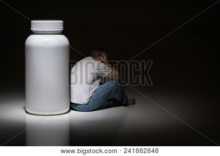 Man Holding Head Sitting Next To Blank Medication Bottle.