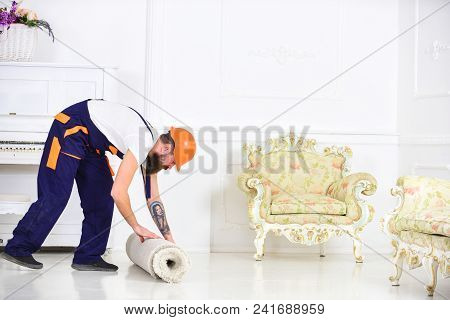 Relocating Concept. Man With Beard, Worker In Overalls And Helmet Rolling Carpet, White Background. 