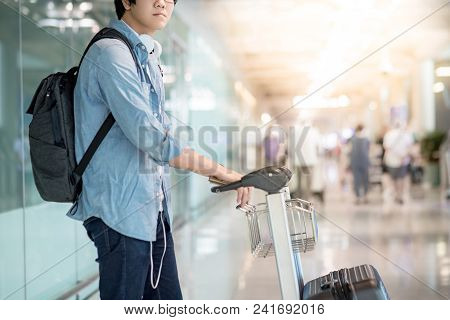 Young Asian Man Walking With Airport Trolley And His Suitcase Luggage In The International Airport T