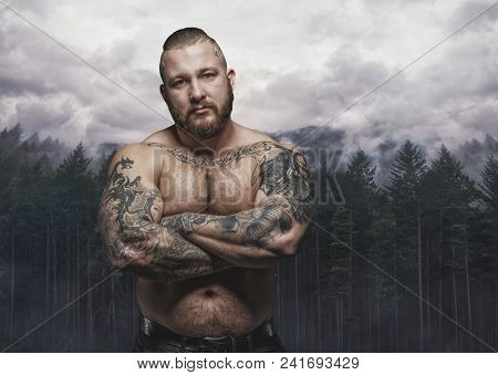 Serious Tattooed Male Over Dark Forest And Cloudy Sky.