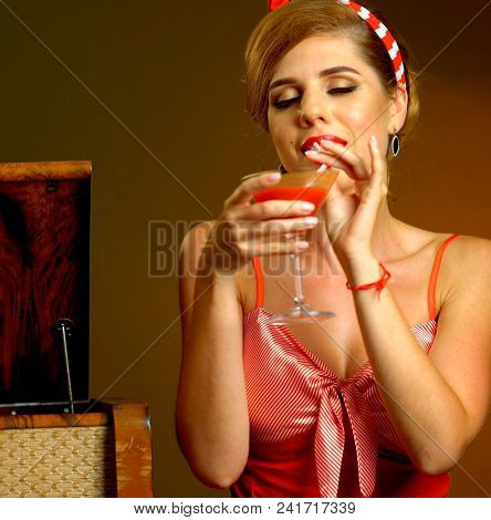 Kiss blow of pin up girl drink bloody Mary cocktail. Pin-up retro female style. Girl pin-up style wearing red dress and wind blowing. Clothes and images of yesteryear.