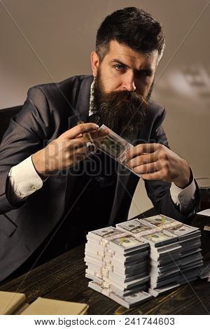 Elegant Man In Suit. Man Sitting At Table With Piles Of Money, Counting Profit. Illegal Cash Concept