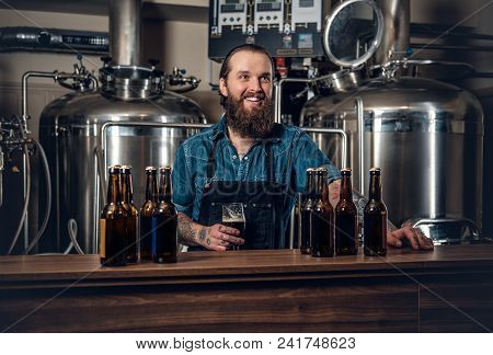 Portrait Of Tattooed, Bearded Hipster Male Manufacturer Presenting Beer Microbrewery.