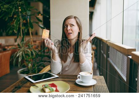 Woman Sitting Near Big Window In Coffee Shop At Table With Credit Card, Cup Of Coffee, Cake, Relaxin