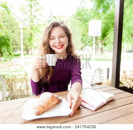 Beautiful Attractive Young Blonde Woman With Curly Hair Drinking Cappuccino And Eating Croissant In 